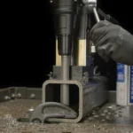 Worker using power tool on metal workpiece.