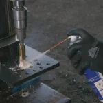 Hand using spray lubricator on metal machining tool.