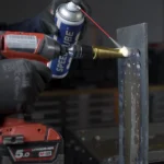 Person using a spray can and drill on metal.